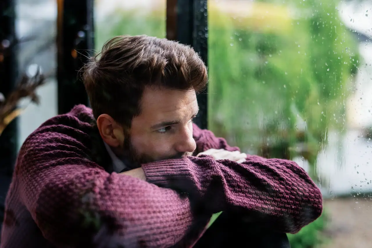 trastorno afectivo estacional, hombre mirando por la ventana con lluvia en invierno