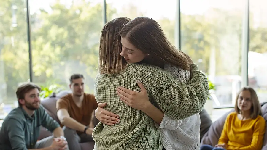 Grupo de personas en círculo terapéutico, con dos mujeres abrazándose en señal de apoyo emocional y prevención del suicidio