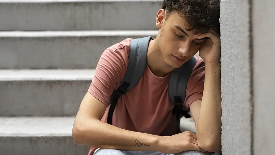 estudiante joven sentado en escaleras con expresión de tristeza y preocupación